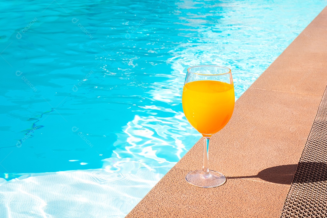 O suco de laranja na taça de vinho fica ao lado da piscina.