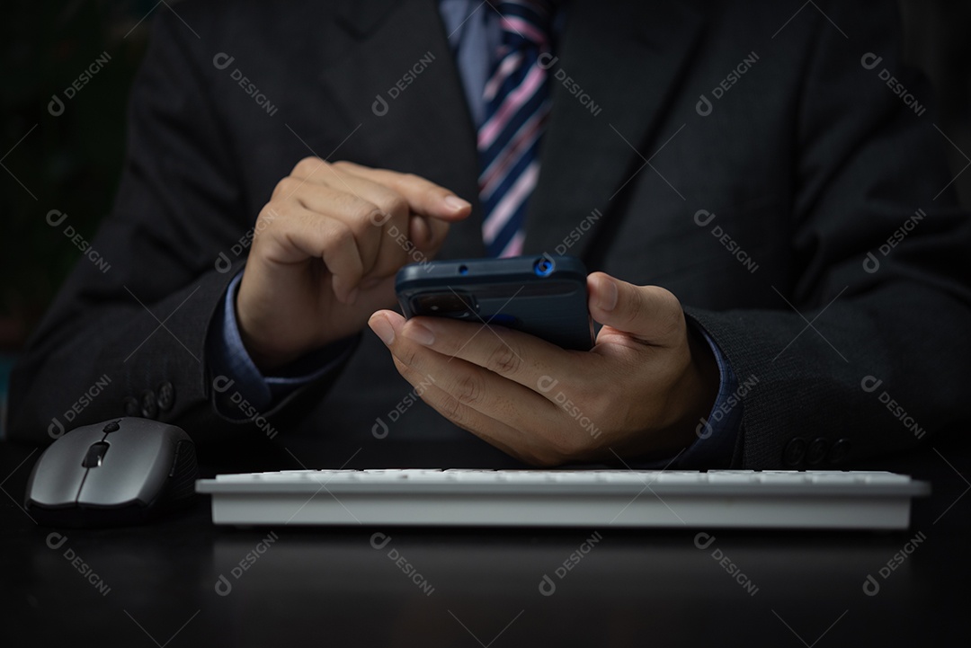 Homem de negócios segurando smartphone móvel e computador de teclado na mesa.