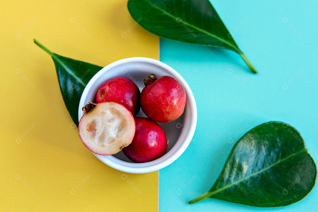 Goiaba cereja vermelha e folhas sobre fundo verde e amarelo