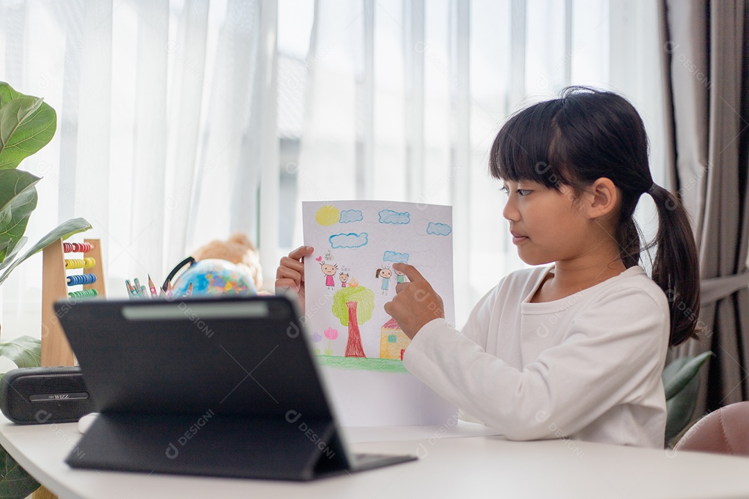 Aluna asiática fazendo sua lição de casa com tablet digital em casa. As crianças usam aparelhos para estudar. Educação e ensino a distância para crianças. Educação domiciliar durante a quarentena. Ficar em casa