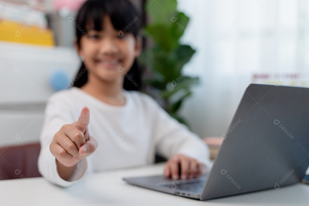Aluna asiática fazendo sua lição de casa com o laptop em casa. As crianças usam aparelhos para estudar. Educação e ensino a distância para crianças. Educação domiciliar durante a quarentena. Ficar em casa
