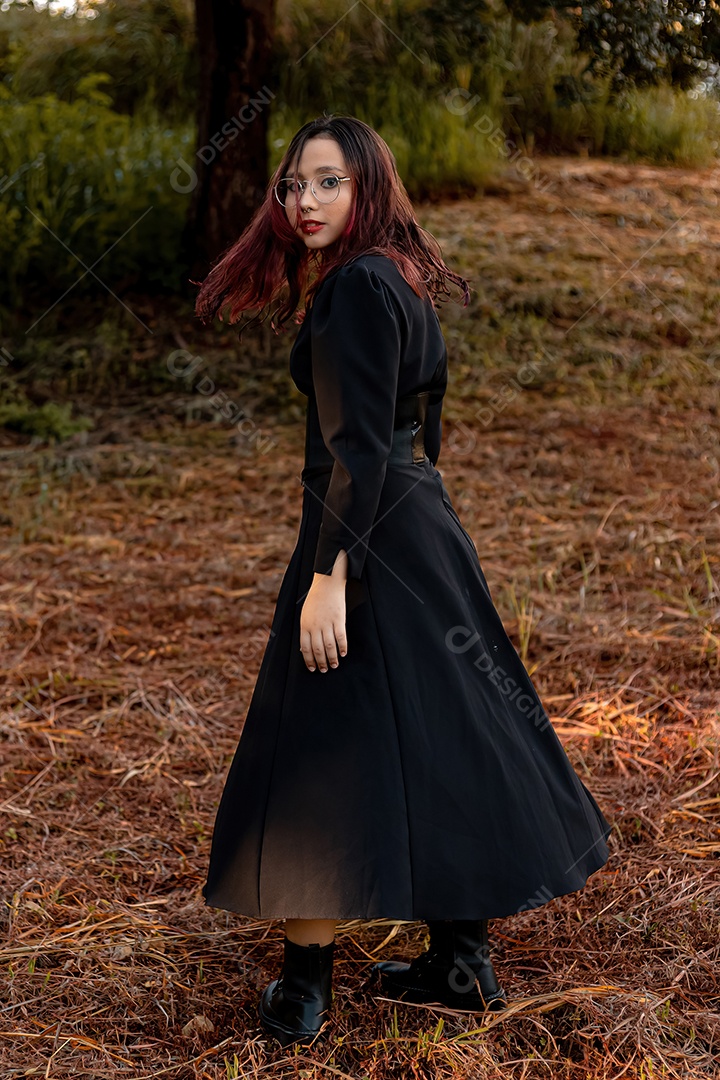 Jovem caucasiana de cabelos escuros com listras vermelhas em roupa de vestido preto com cinto espartilho e óculos posando para sessão de beleza feminina