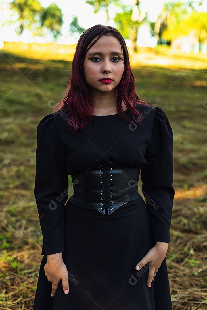 Jovem caucasiana de cabelos escuros com listras vermelhas em roupa de vestido preto com cinto espartilho e óculos posando para sessão de beleza feminina