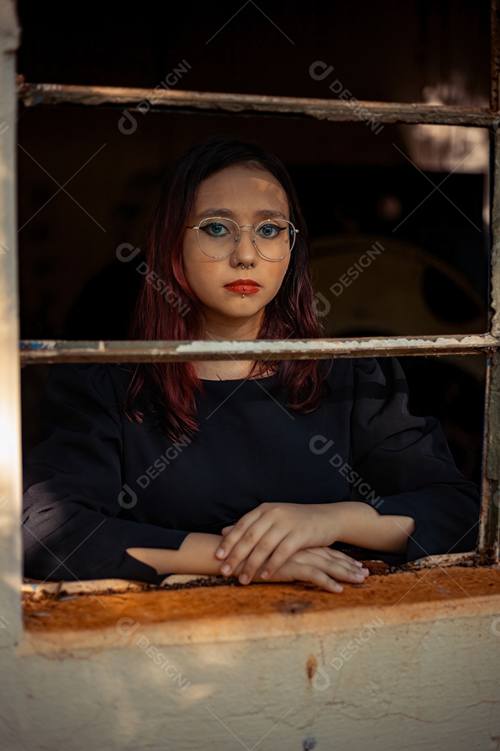 Jovem caucasiana de cabelos escuros com listras vermelhas em roupa de vestido preto com cinto espartilho e óculos posando para sessão de beleza feminina