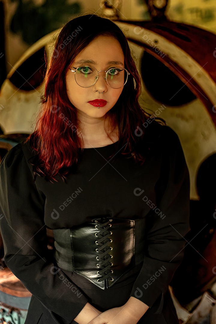 Jovem caucasiana de cabelos escuros com listras vermelhas em roupa de vestido preto com cinto espartilho e óculos posando para sessão de beleza feminina