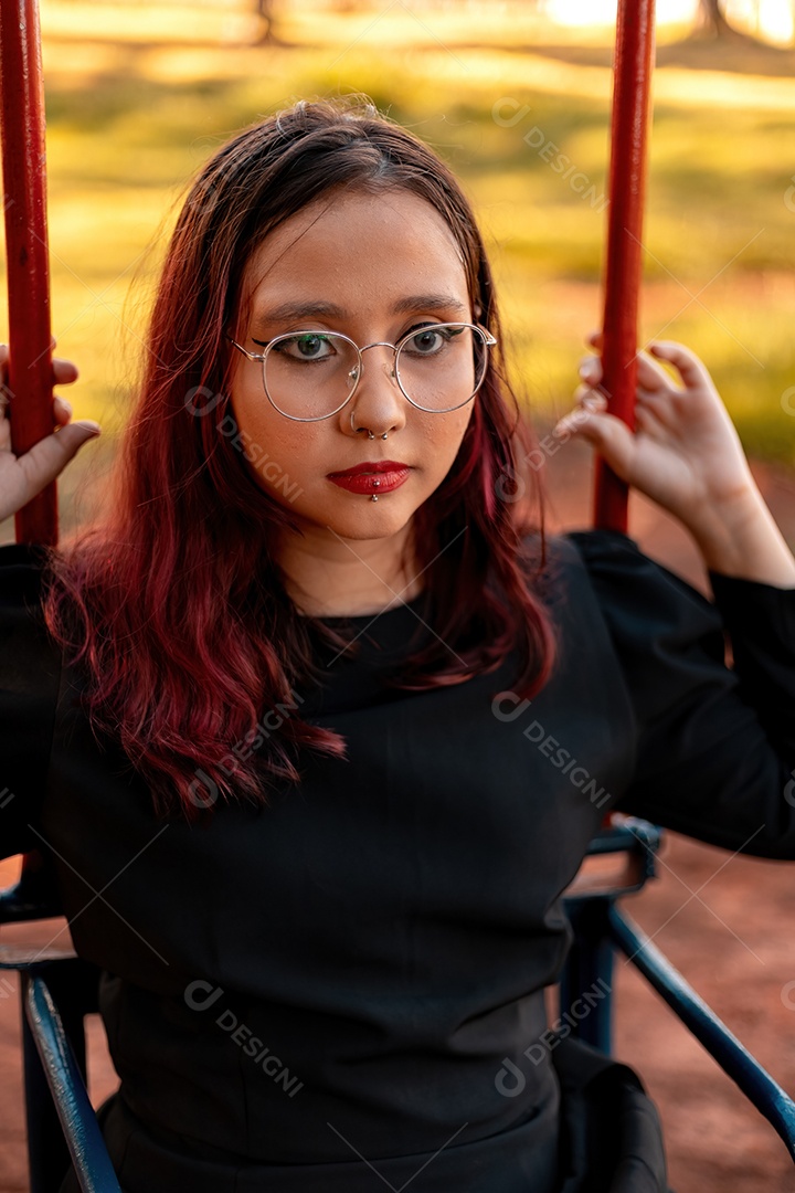 Jovem caucasiana de cabelos escuros com listras vermelhas em roupa de vestido preto com cinto espartilho e óculos posando para sessão de beleza feminina