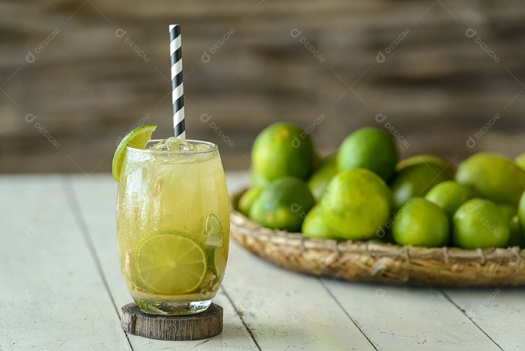 Bebida brasileira Caipirinha em uma mesa de madeira branca com limões ao fundo.