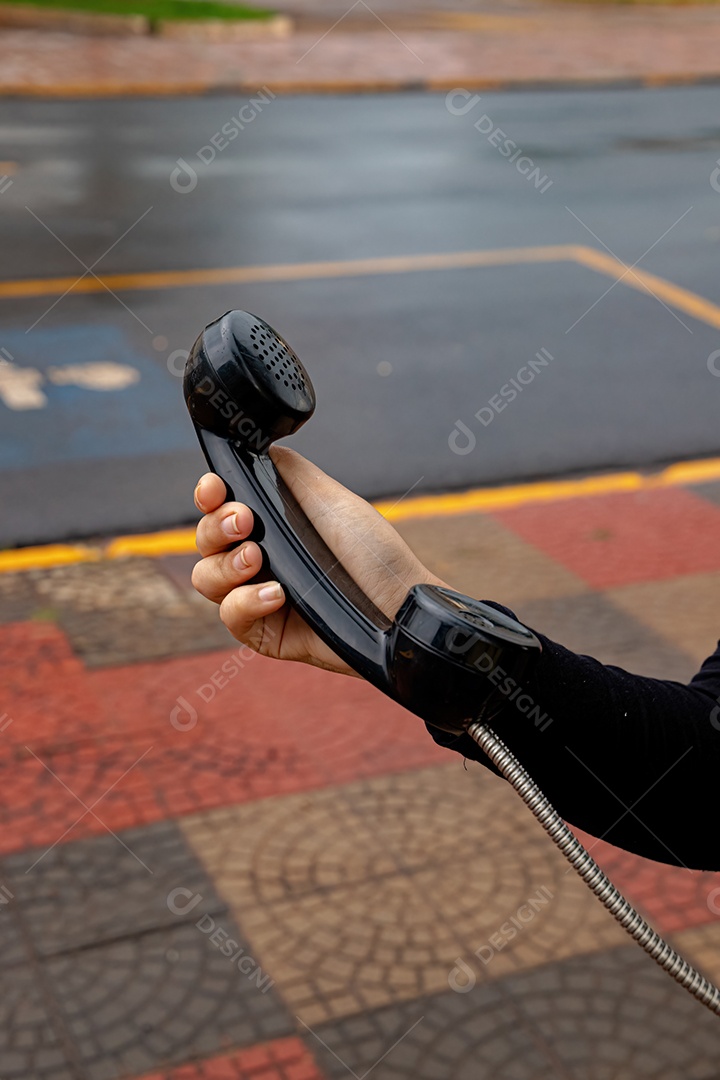 Telefone preto de um orelhão público sendo segurado por uma mulher