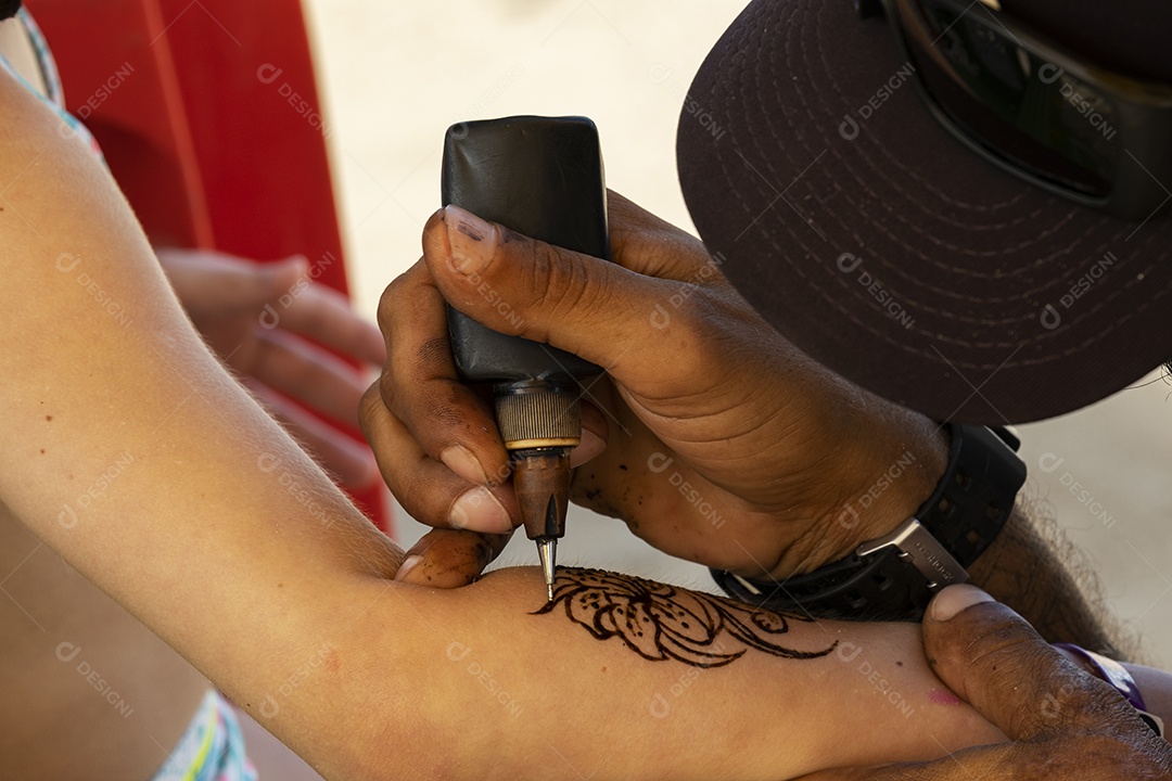 Tatuador fazendo tatuagem de henna no braço de uma menina