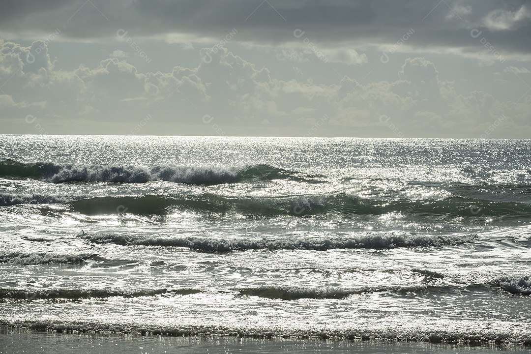 ondas do mar vistas ao entardecer, refletindo a luminosidade do sol.