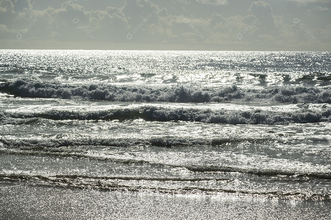 ondas do mar vistas ao entardecer, refletindo a luminosidade do sol.