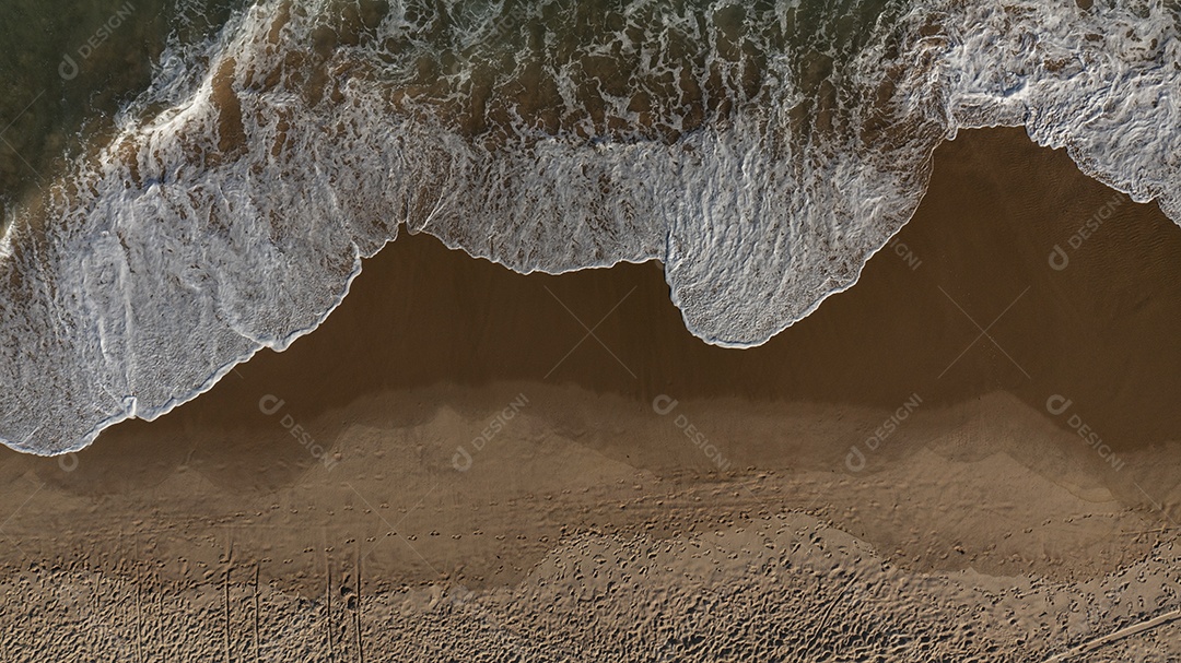 vista superior da onda formando espuma quando atinge a areia da praia