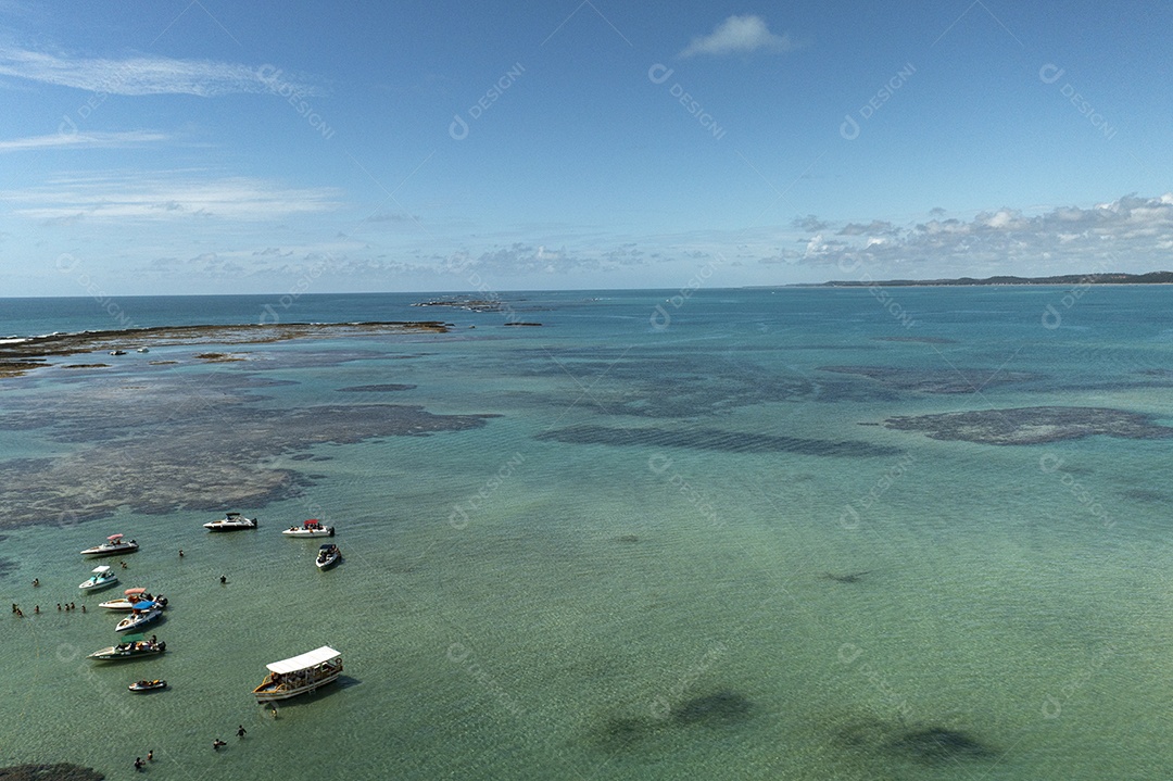 turistas e pequenos barcos em uma piscina natural formada por arrecifes