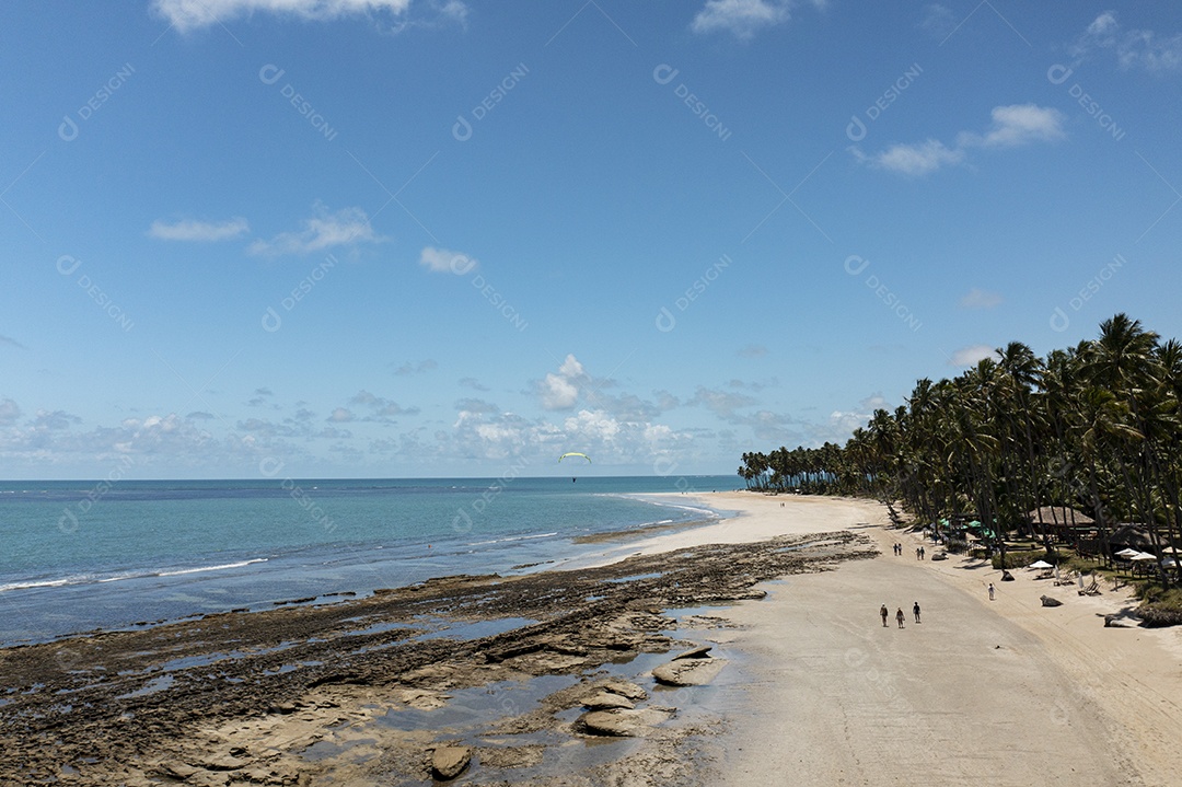 turistas caminhando pela praia com recifes entre a praia e o mar na maré baixa.