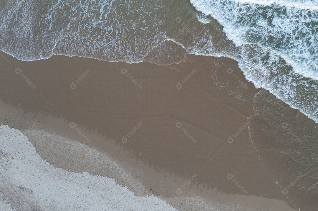vista superior da onda quebrando na areia, deixando-a com tonalidades diferentes