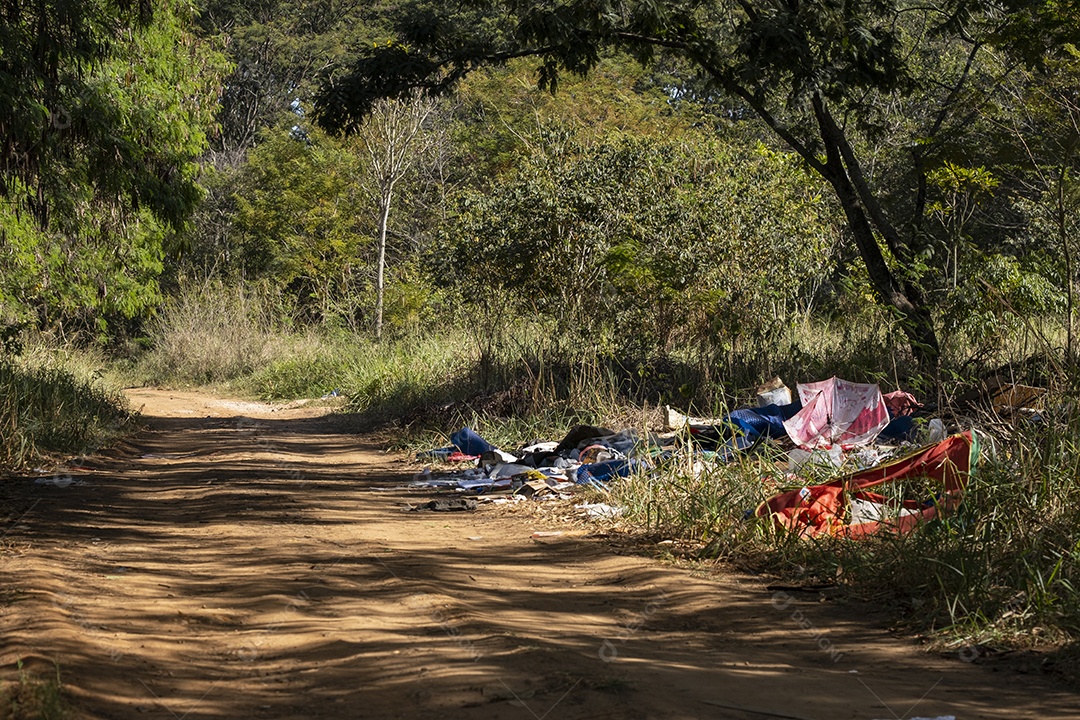 lixo deixado na beira de uma estrada de terra próximo a mata