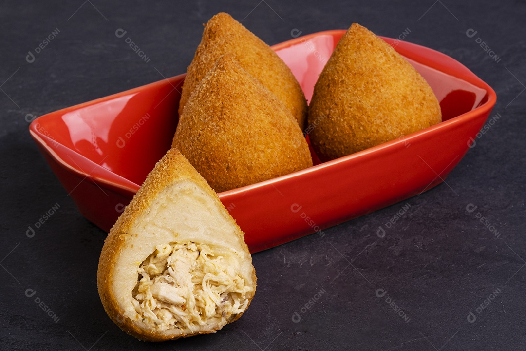 coxinha frita tradicional em um recipiente vermelho em uma pedra de ardósia.