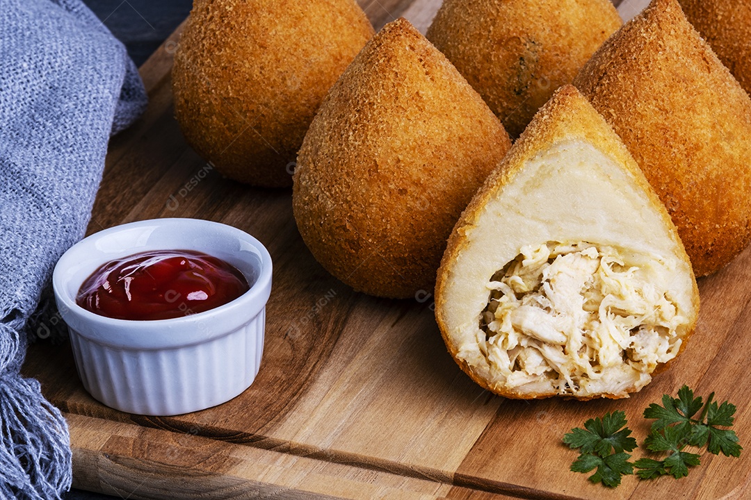 coxinhas fritas tradicionais em uma tábua de madeira e uma panela de ketchup.