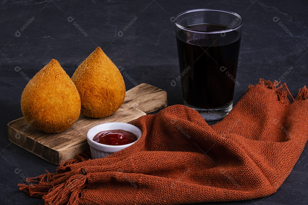 Tradicional coxinha frita recheada com frango e um copo de refrigerante gelado.