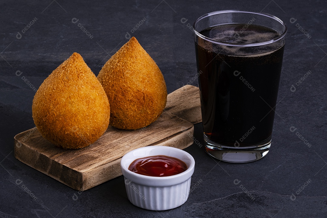 Tradicional coxinha frita recheada com frango e um copo de refrigerante gelado.