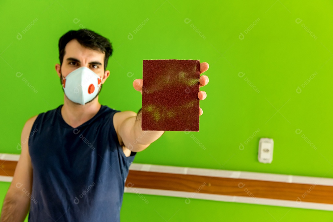 Homem segurando uma lixa depois de lixar a parede verde