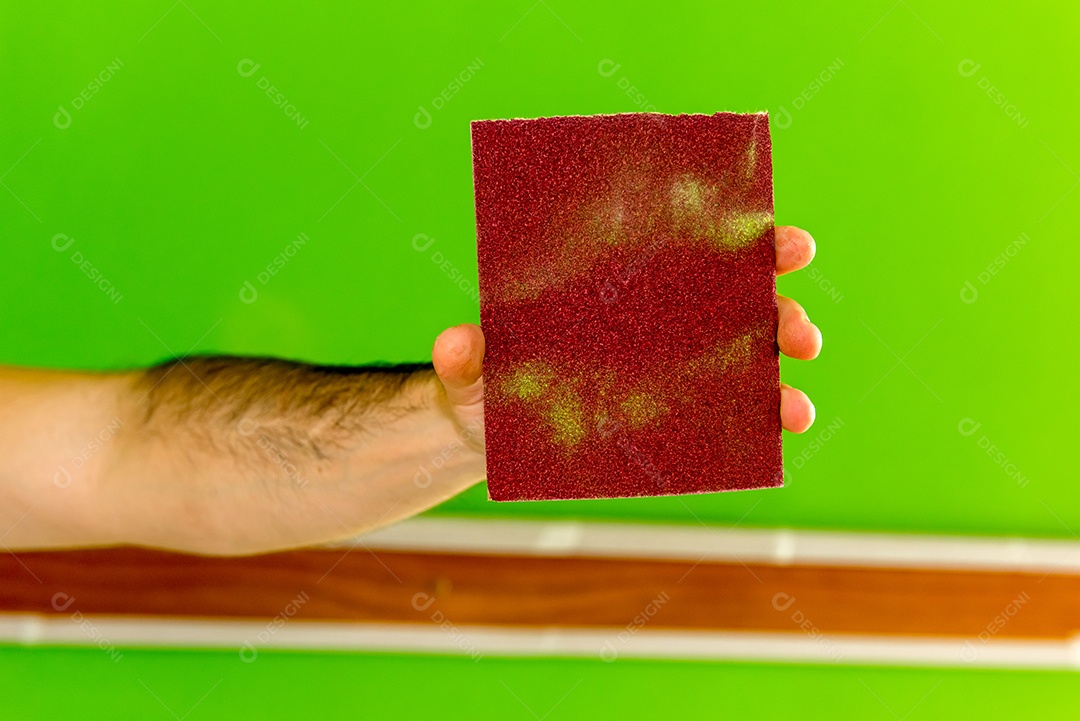 Homem segurando uma lixa depois de lixar a parede verde