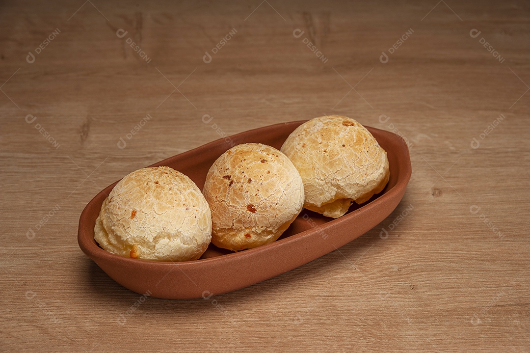 Pães de queijo em um ramekin verde na mesa de madeira e fundo da parede de tijolos.