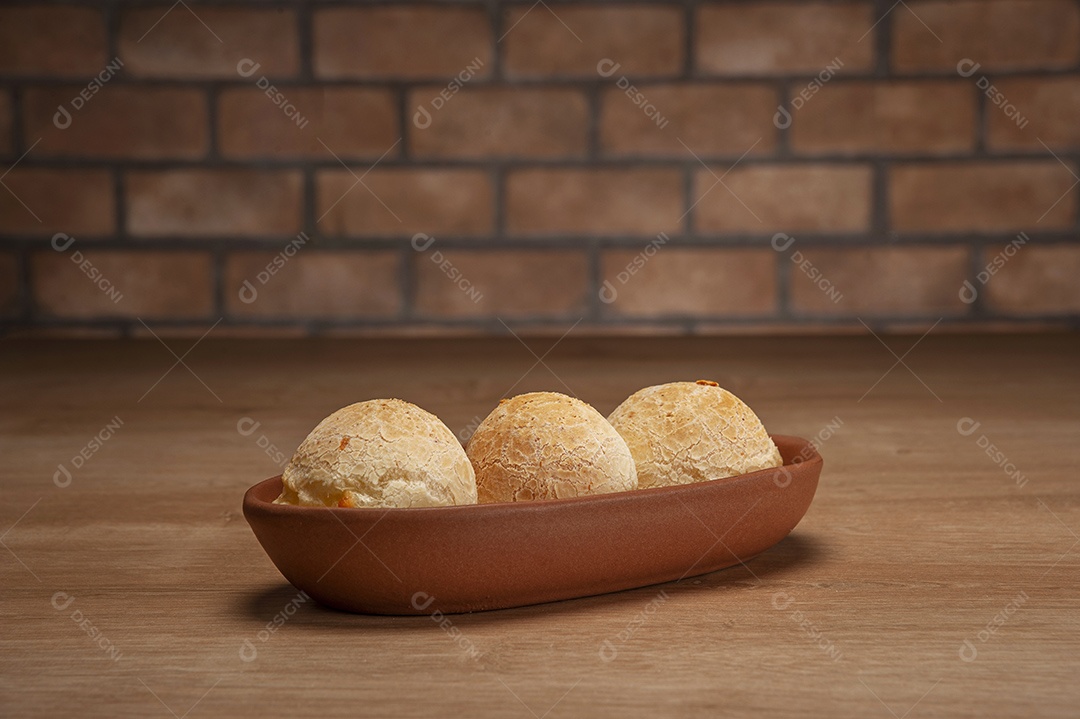 Pães de queijo em um ramekin verde na mesa de madeira e fundo da parede de tijolos.
