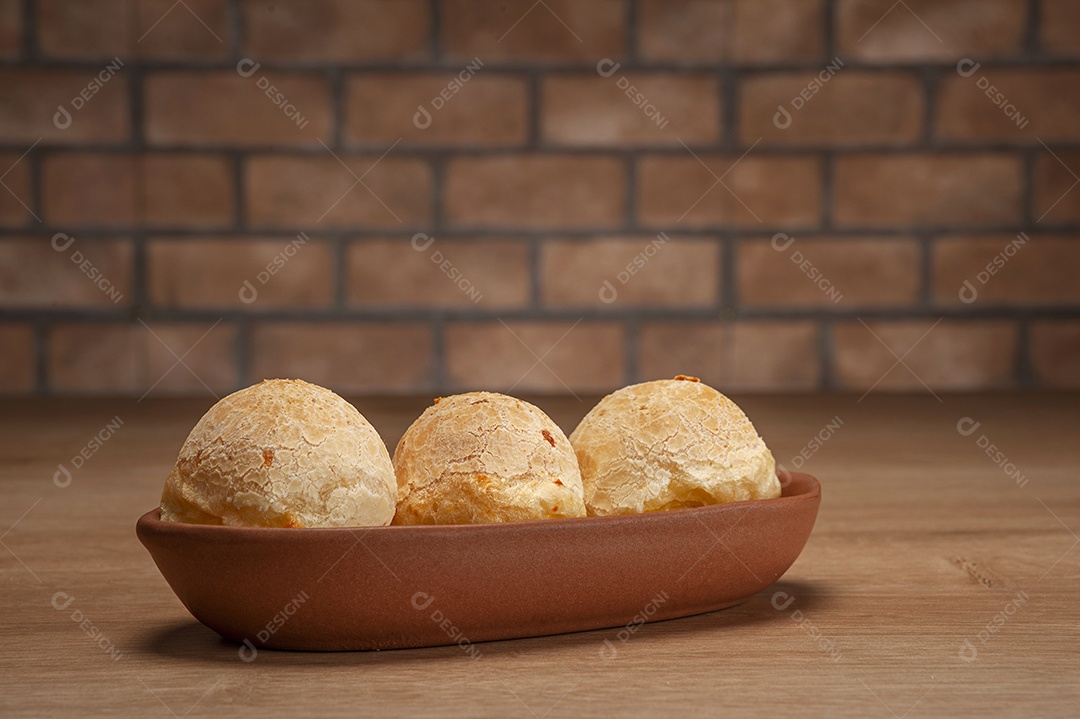 Pães de queijo em um ramekin verde na mesa de madeira e fundo da parede de tijolos.