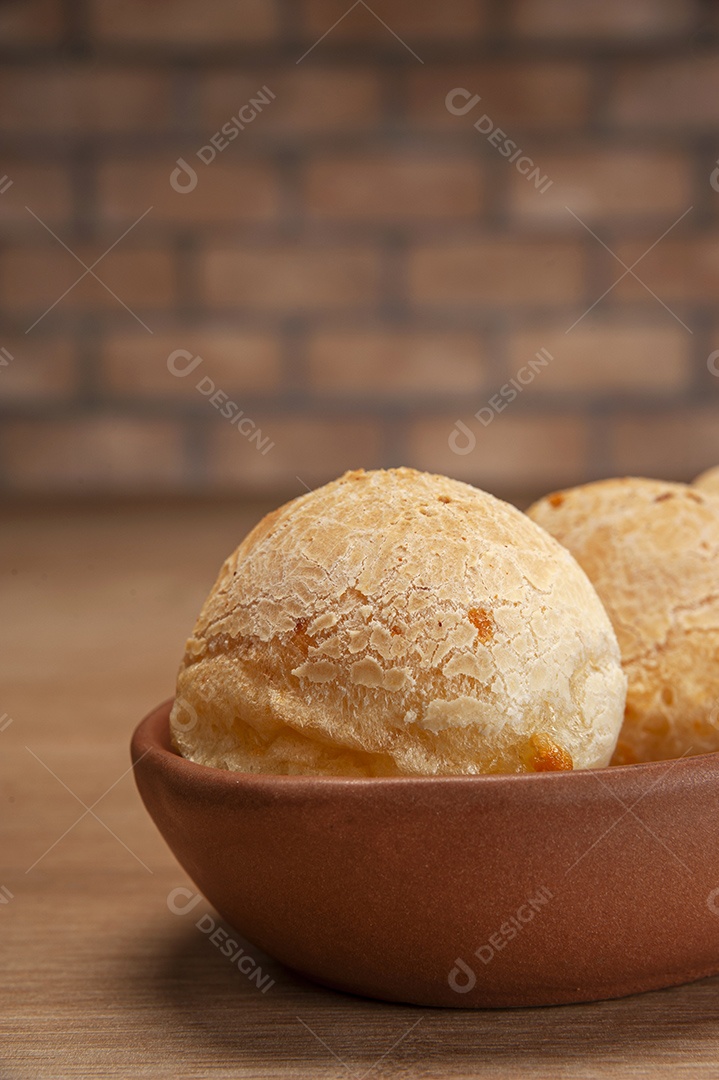 Pães de queijo em um ramekin verde na mesa de madeira e fundo da parede de tijolos.