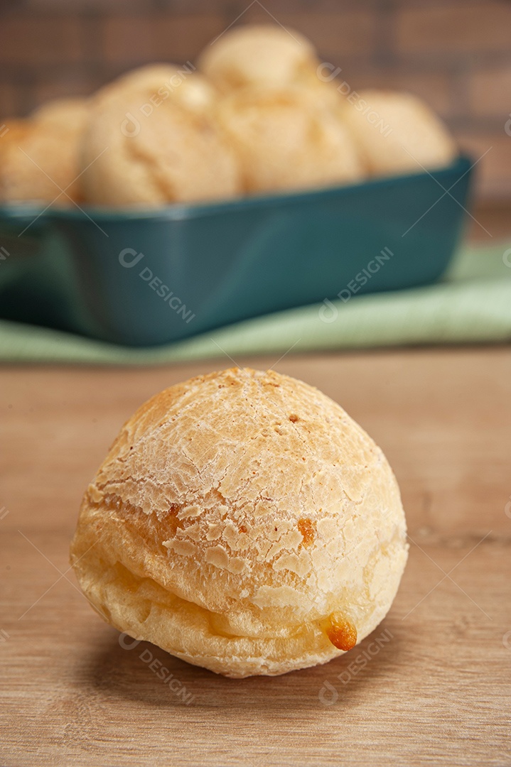 Pães de queijo em um ramekin verde na mesa de madeira e fundo da parede de tijolos.
