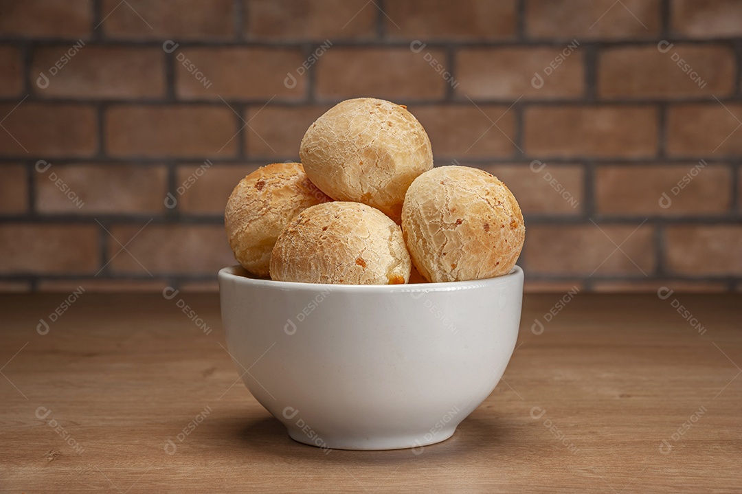 Pães de queijo em um ramekin verde na mesa de madeira e fundo da parede de tijolos.
