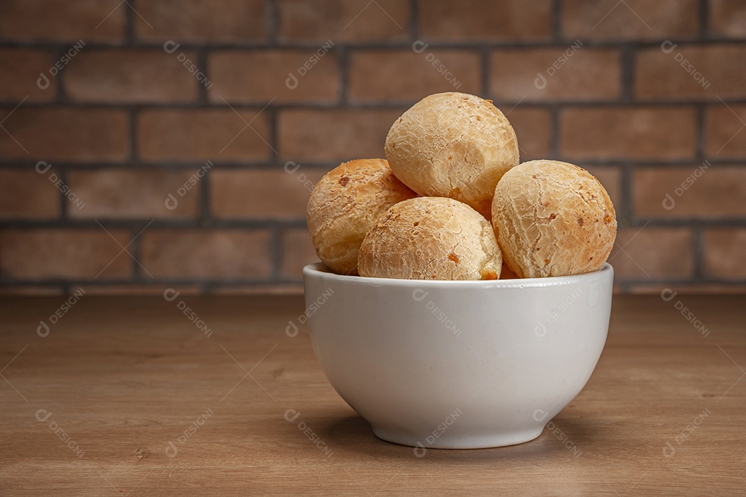 Pães de queijo em um ramekin verde na mesa de madeira e fundo da parede de tijolos.