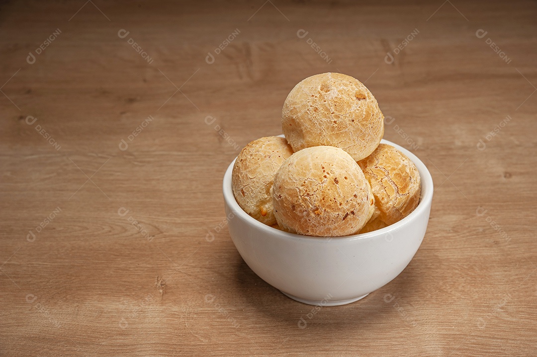 Pães de queijo em um ramekin verde na mesa de madeira e fundo da parede de tijolos.