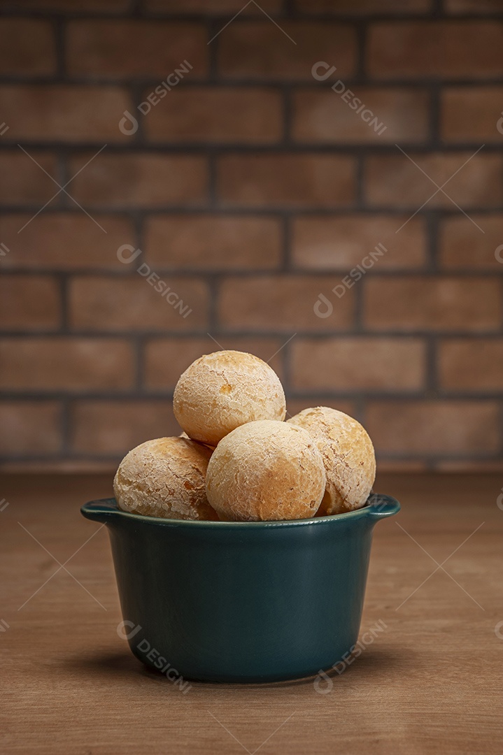 Pães de queijo em um ramekin verde na mesa de madeira e fundo da parede de tijolos.