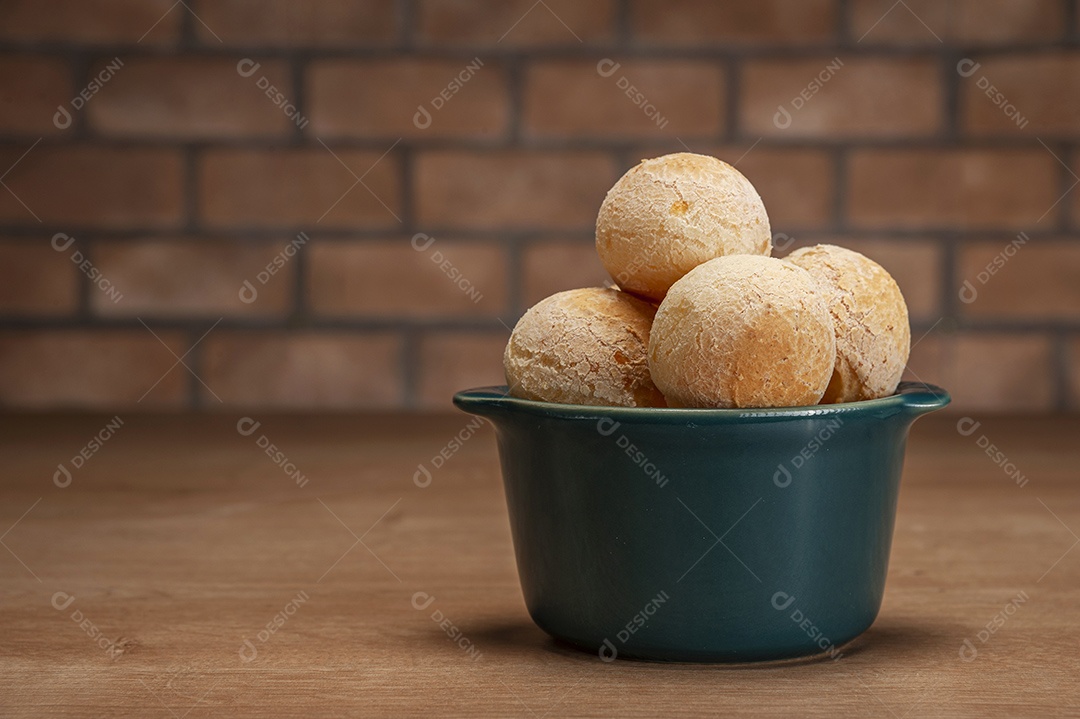 Pães de queijo em um ramekin verde na mesa de madeira e fundo da parede de tijolos.