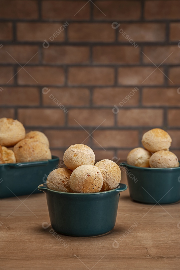 Pães de queijo em um ramekin verde na mesa de madeira e fundo da parede de tijolos.