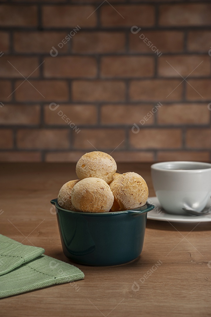 Pães de queijo em um ramekin verde na mesa de madeira e fundo da parede de tijolos.