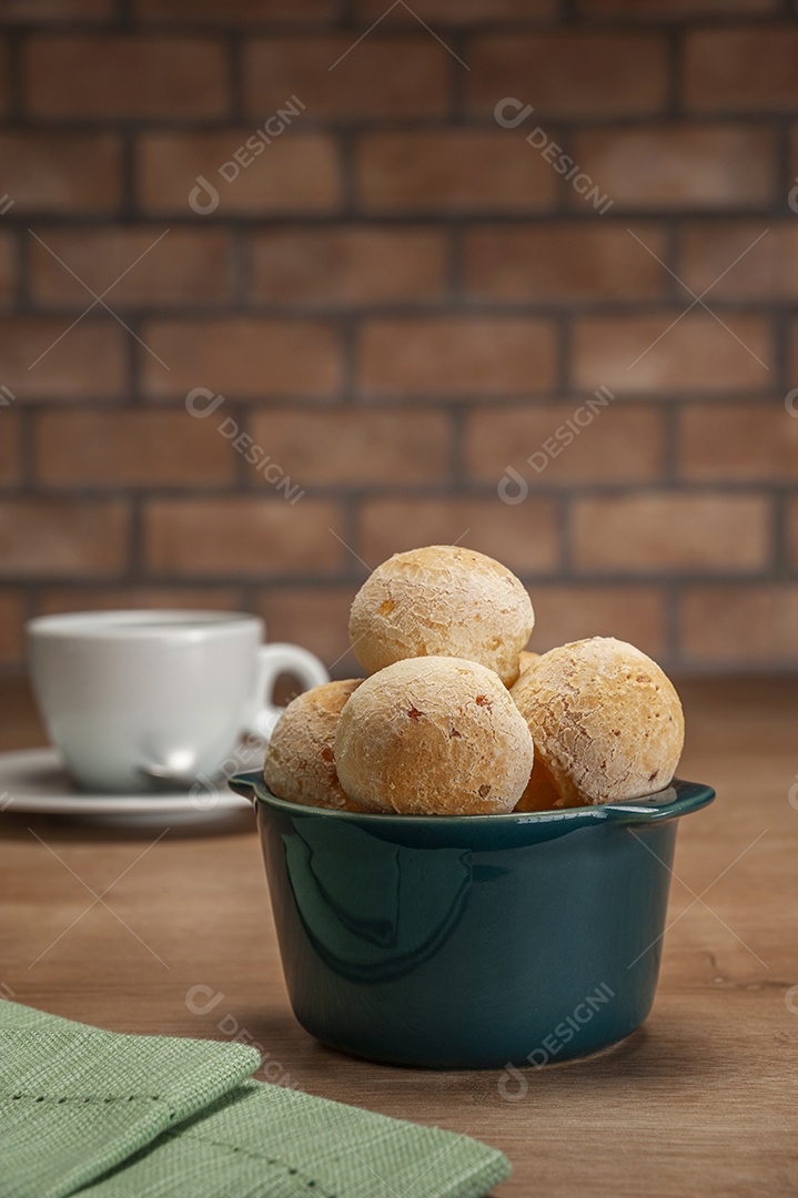 Pães de queijo em um ramekin verde na mesa de madeira e fundo da parede de tijolos.