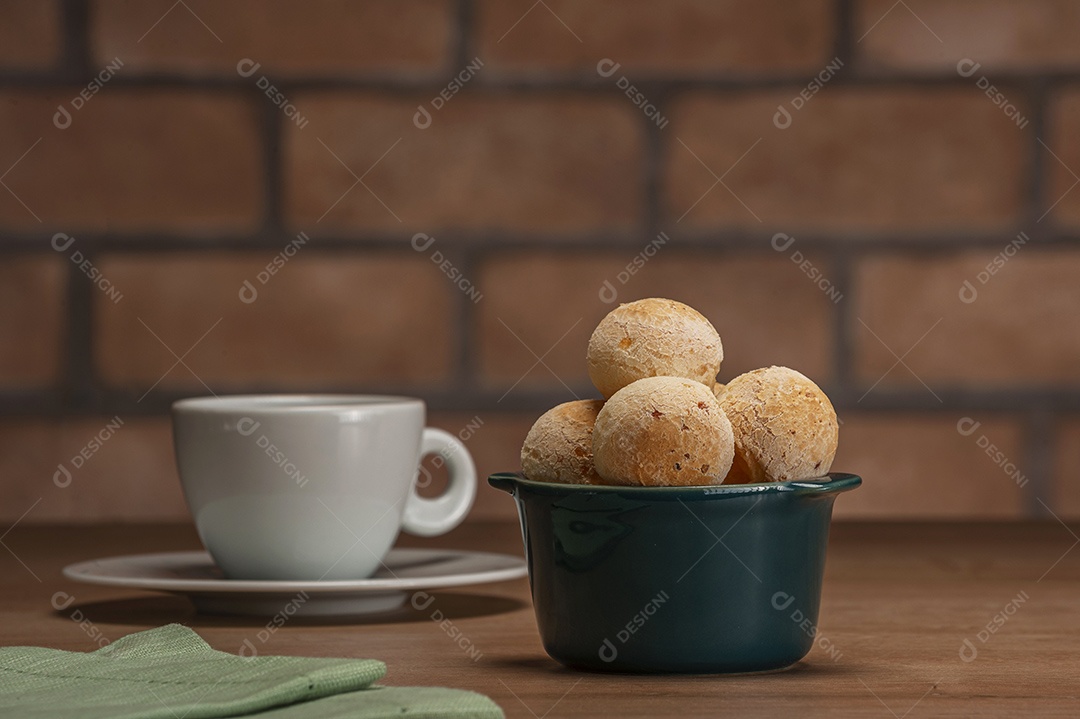 Pães de queijo em um ramekin verde na mesa de madeira e fundo da parede de tijolos.