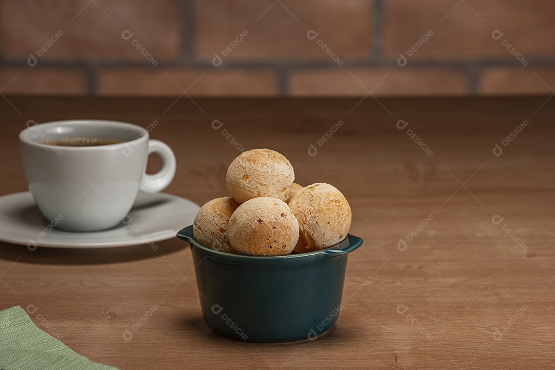 Pães de queijo em um ramekin verde na mesa de madeira e fundo da parede de tijolos.