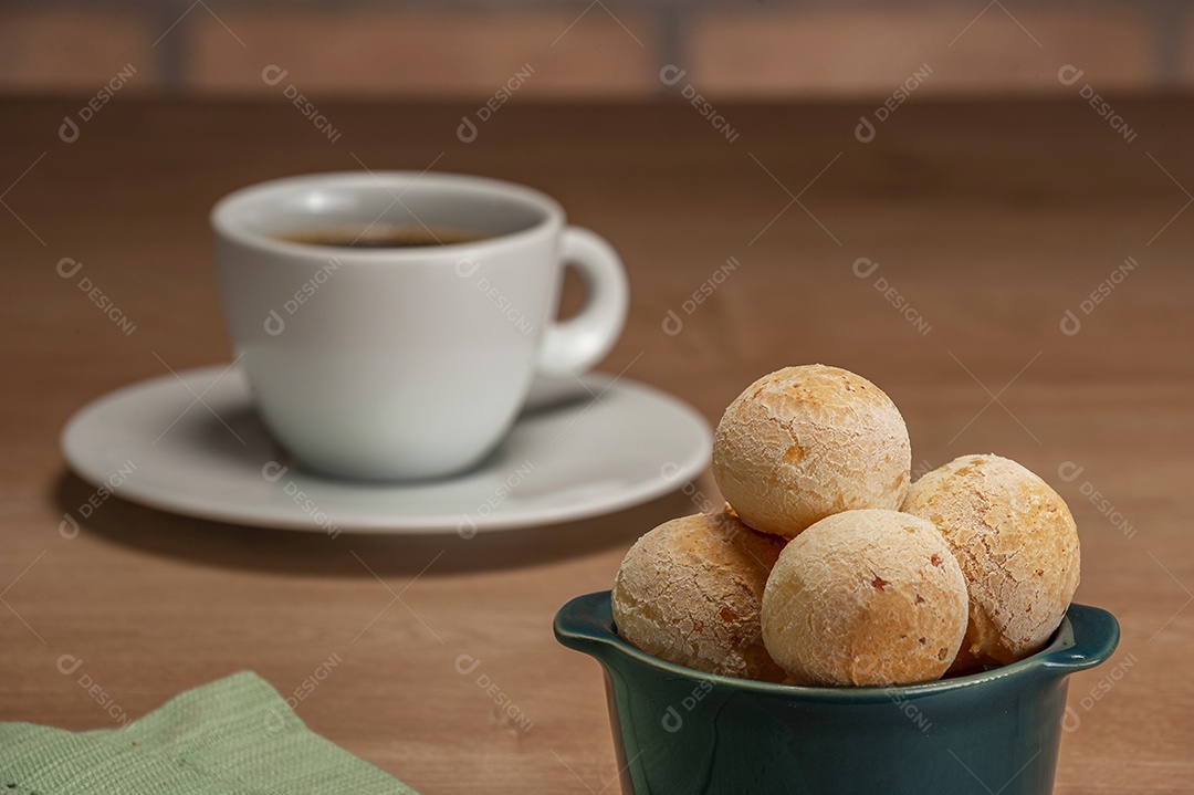 Pães de queijo em um ramekin verde na mesa de madeira e fundo da parede de tijolos.