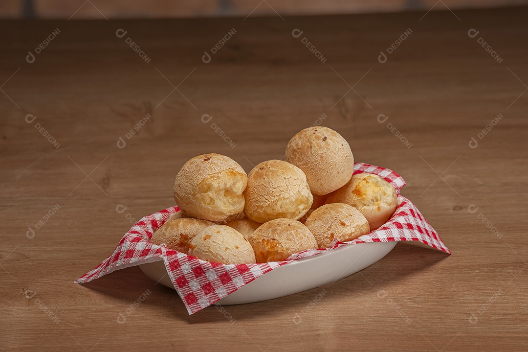 Pães de queijo em um ramekin verde na mesa de madeira e fundo da parede de tijolos.