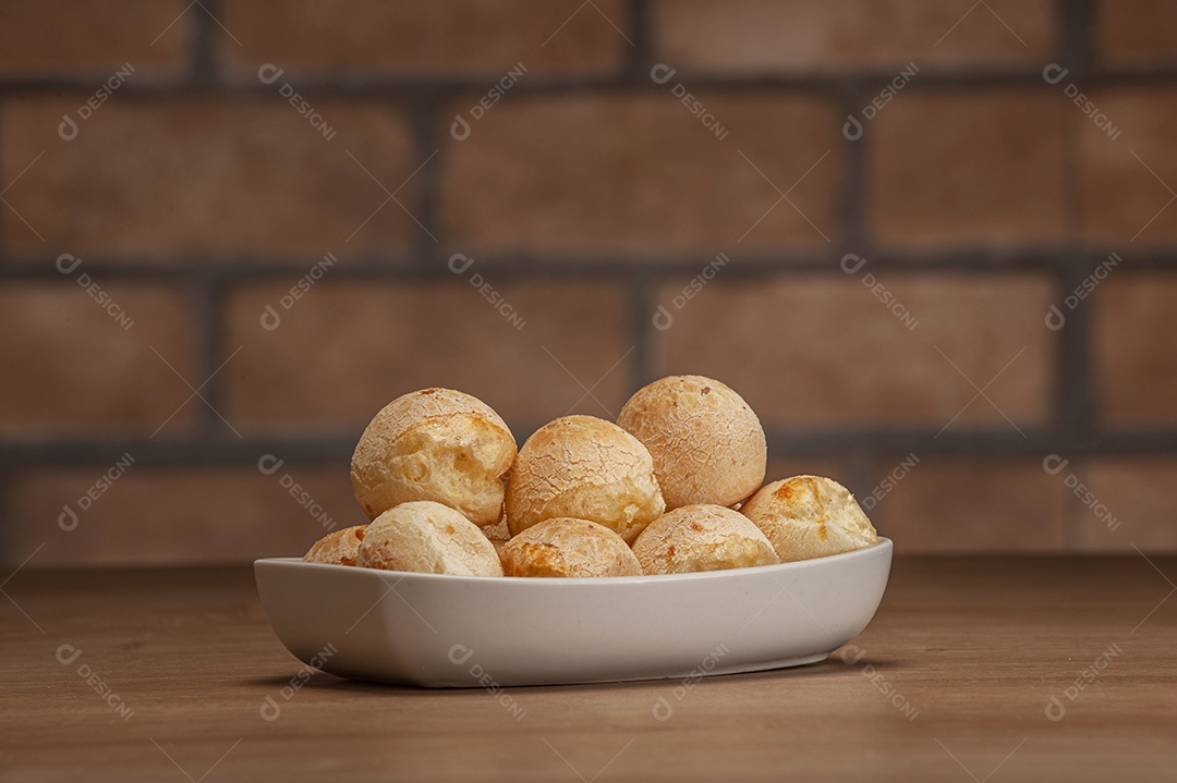 Pães de queijo em um ramekin verde na mesa de madeira e fundo da parede de tijolos.