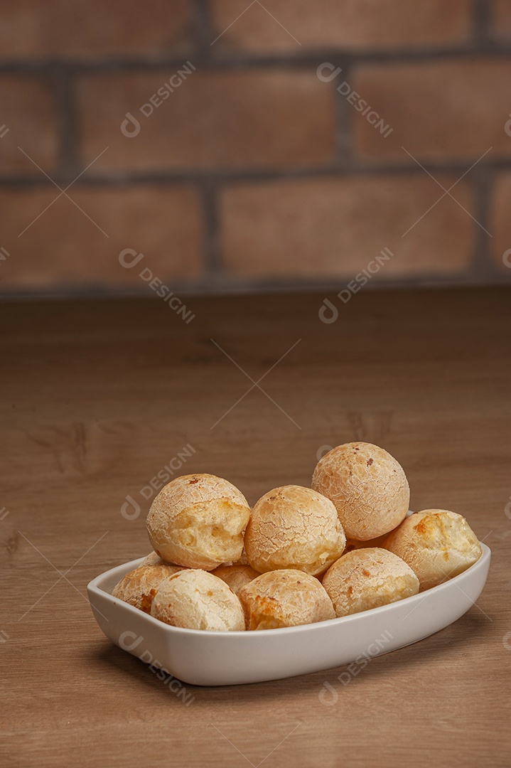 Pães de queijo em um ramekin verde na mesa de madeira e fundo da parede de tijolos.