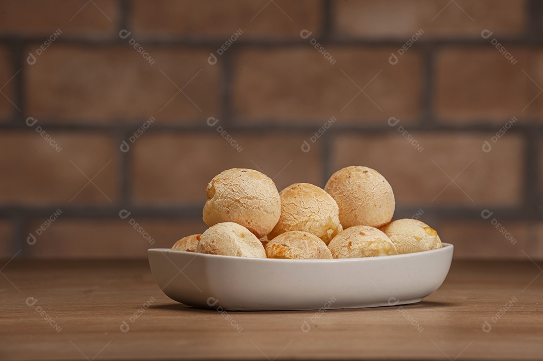 Pães de queijo em um ramekin verde na mesa de madeira e fundo da parede de tijolos.