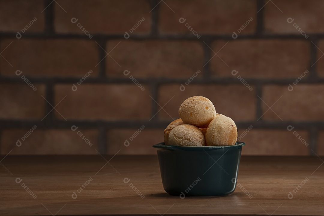 Pães de queijo em um ramekin verde na mesa de madeira e fundo da parede de tijolos.