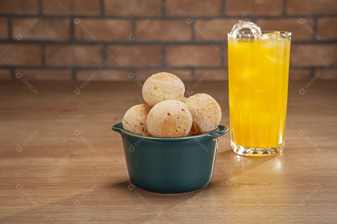 Pães de queijo em um ramekin verde com um copo de suco de laranja na mesa de madeira e fundo de parede de tijolos.
