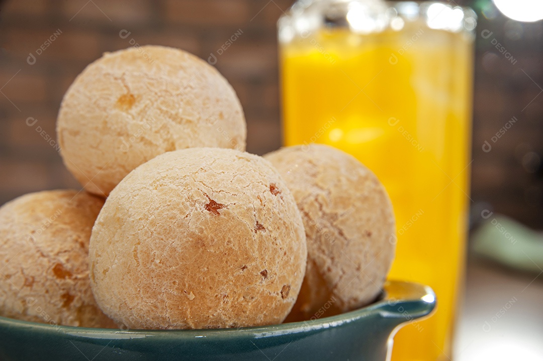 Pães de queijo em um ramekin verde com um copo de suco de laranja na mesa de madeira e fundo de parede de tijolos.