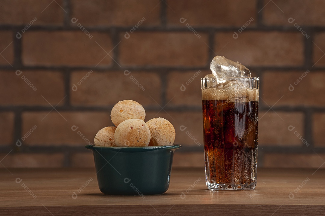 Pães de queijo em um ramekin verde com um copo de refrigerante de cola na mesa de madeira e fundo de parede de tijolos.